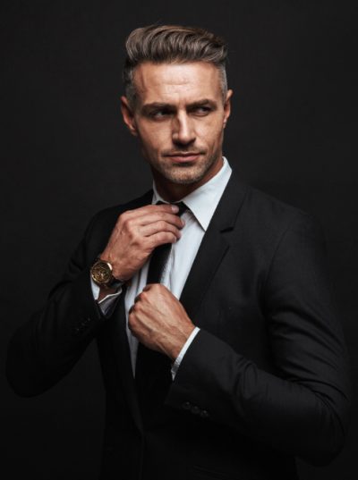 Handsome confident businessman wearing suit standing isolated over black background, posing